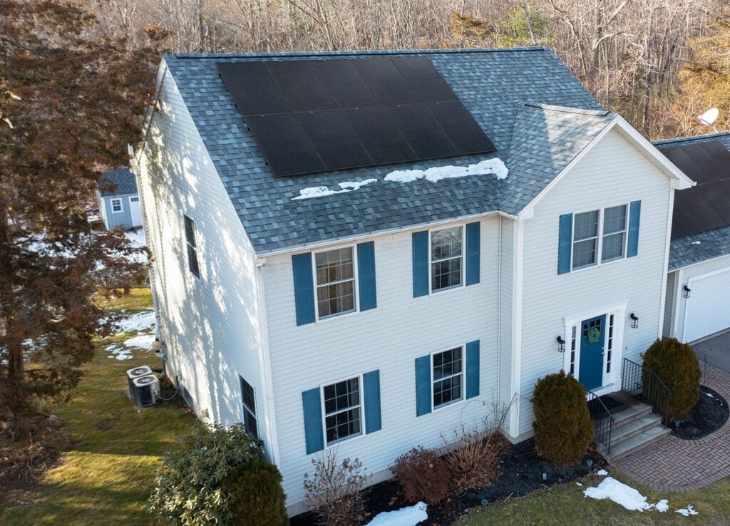 Solar panels installed by Rooftop Power on a cream colonial home with blue shutters and an attached garage.