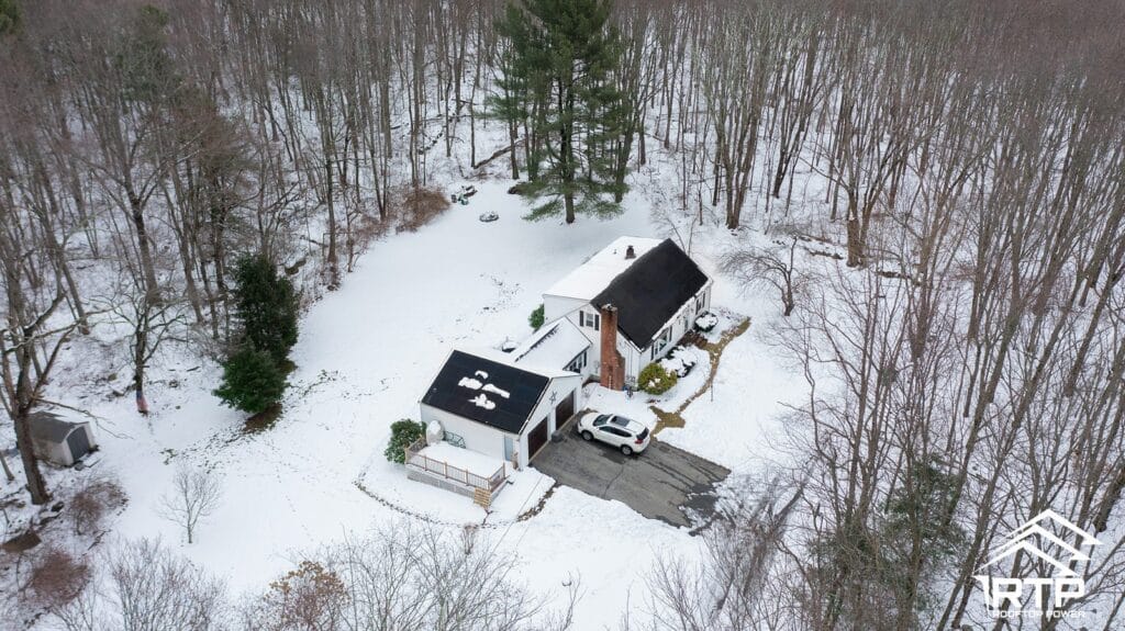 All-black solar panels installed by Rooftop Power on a rural home and detached garage, seen from above with snow on the ground.